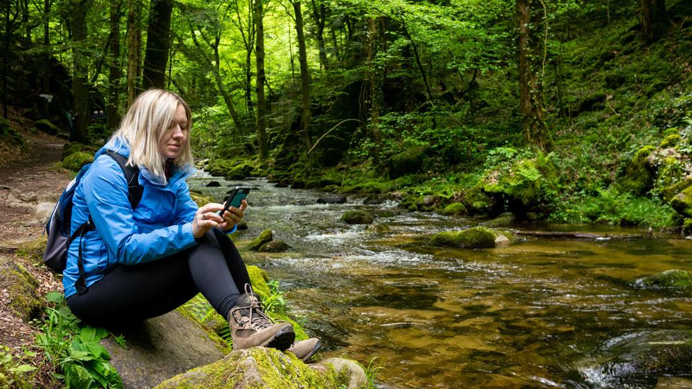 Woman checking phone by a stream